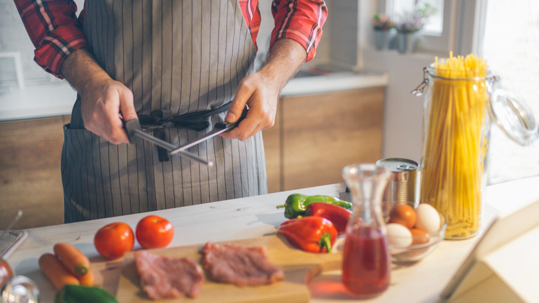Man in the kitchen sharpening a kitchen knife.