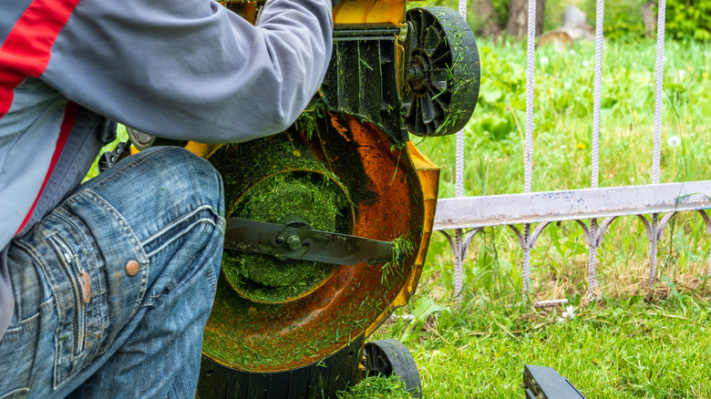 Person cleaning a lawn mower on its side with a clogged deck.
