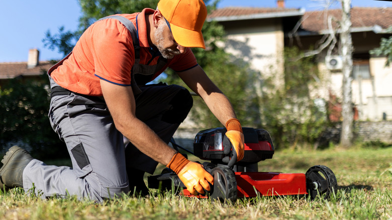 A man raising a walk-behind lawn mower's deck
