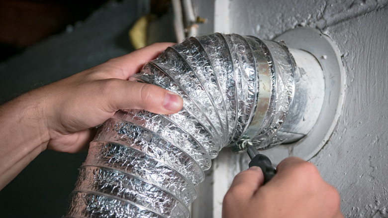 close up of hands removing screw from dryer vent opening