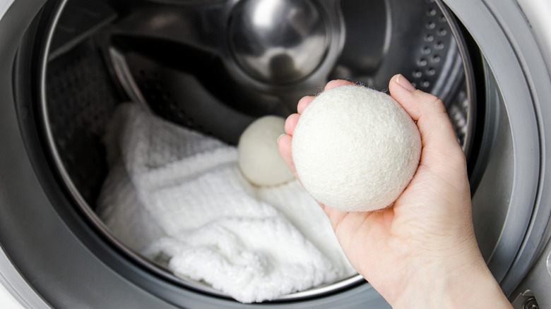 hand holding a wool dryer ball in front of a dryer with blanket and another wool ball inside