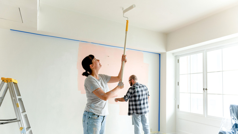 Two people painting a room using a paint roller
