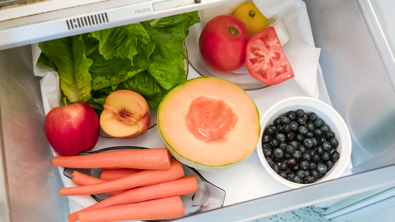 A refrigerator produce drawer is lined with paper towels and filled with colorful fruits and vegetables.