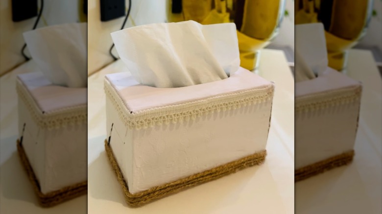 Tissue box decorated with paint, twine, and ribbon.