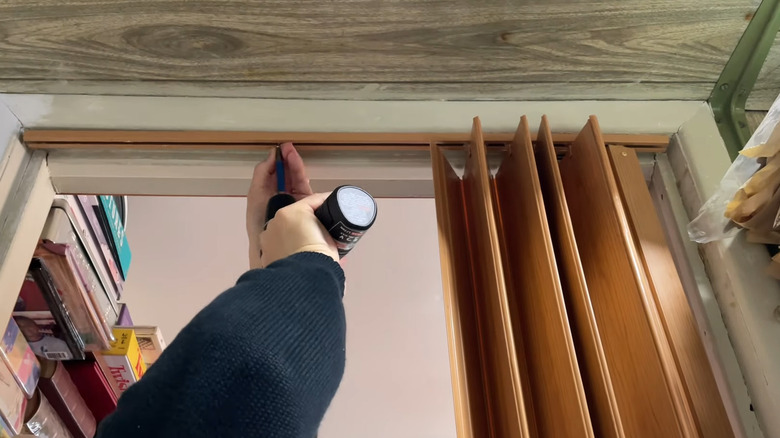 Man drilling panels for wood-like accordion door on upper track