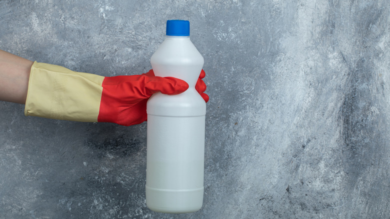 A person holding a bleach bottle with a red glove