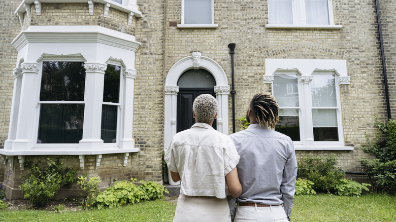 A couple stands facing a historic home