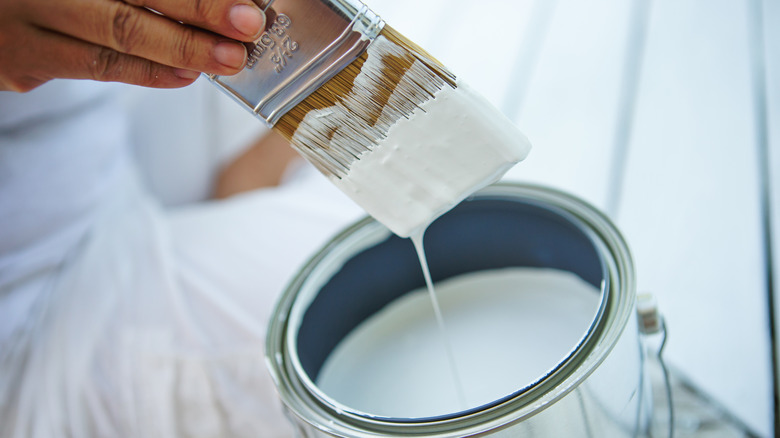 A person dips a paintbrush into a bucket of paint