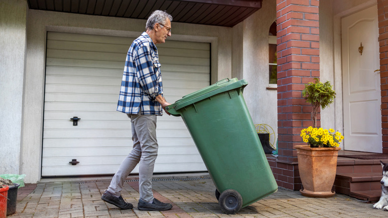 Senior man pushing green trash can outside of home