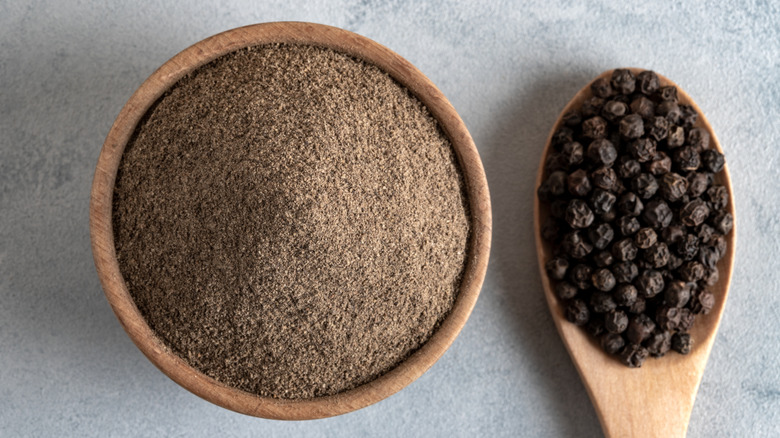 ground black pepper in a bowl and a spoon of peppercorns
