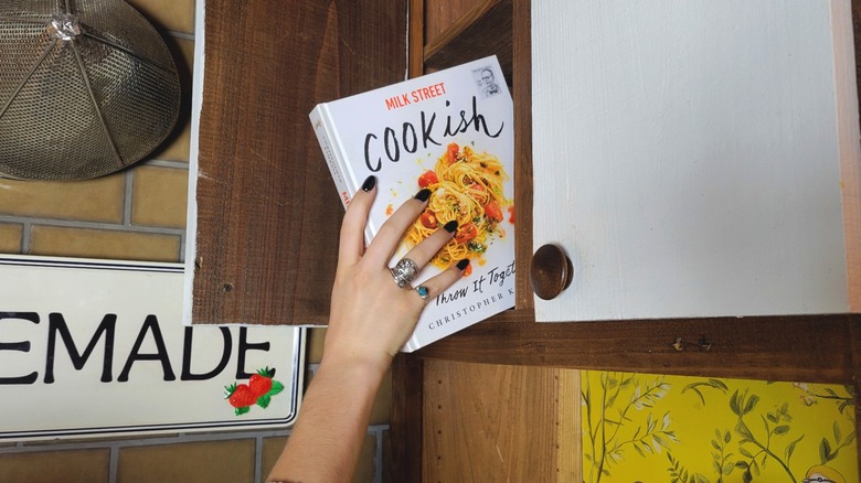 Hand reaching pulling a cookbook from thrifted countertop cabinet