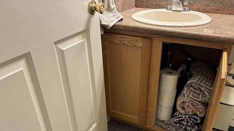 Small bathroom with open cabinet filled with toilet paper and towels