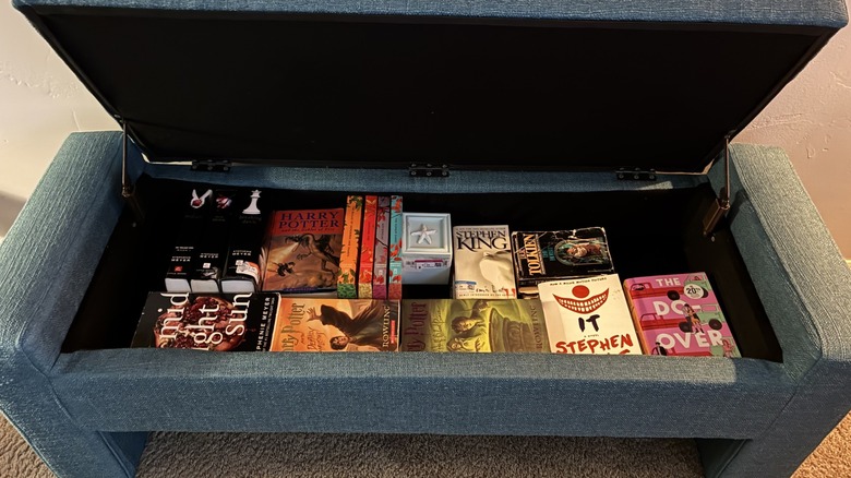 A blue, upholstered storage bench filled with books