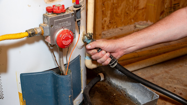 A man's hand is shown connecting a drain hose to a hot water heater