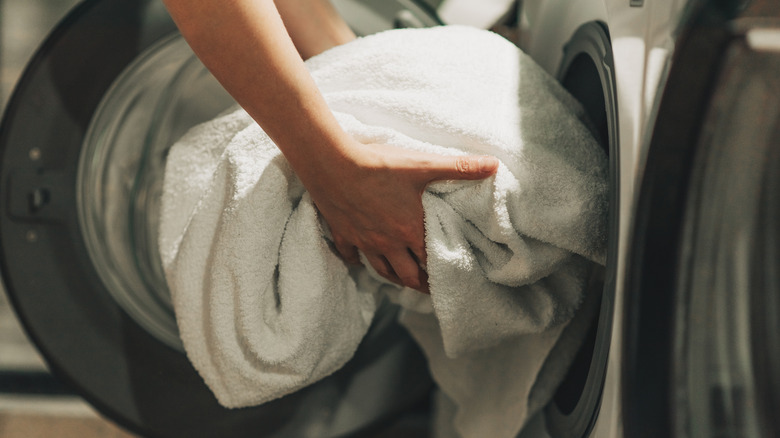 Person placing white towels in a washing machine