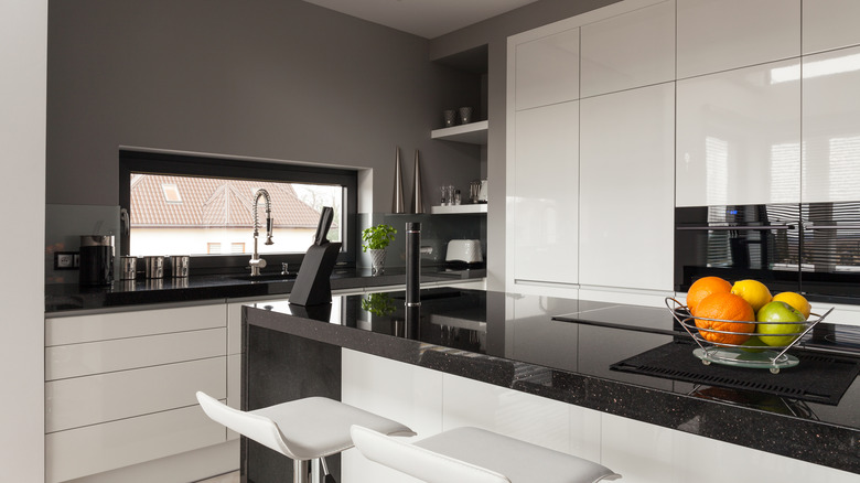 A kitchen with white tile and black counters and window frames