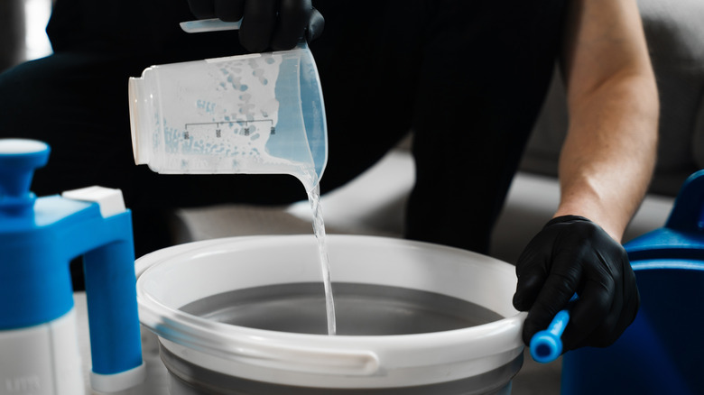 person pouring liquid from a measuring cup into a bucket to mix
