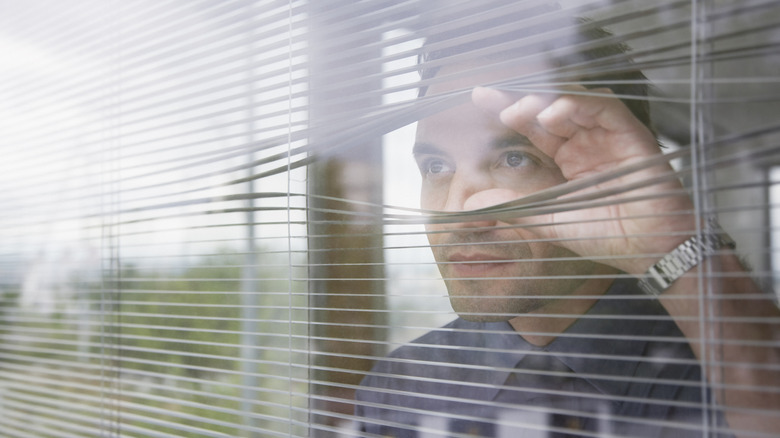 Man spying out his window through the blinds