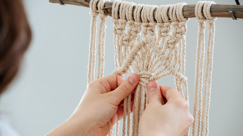 Woman tying macrame on a rod.