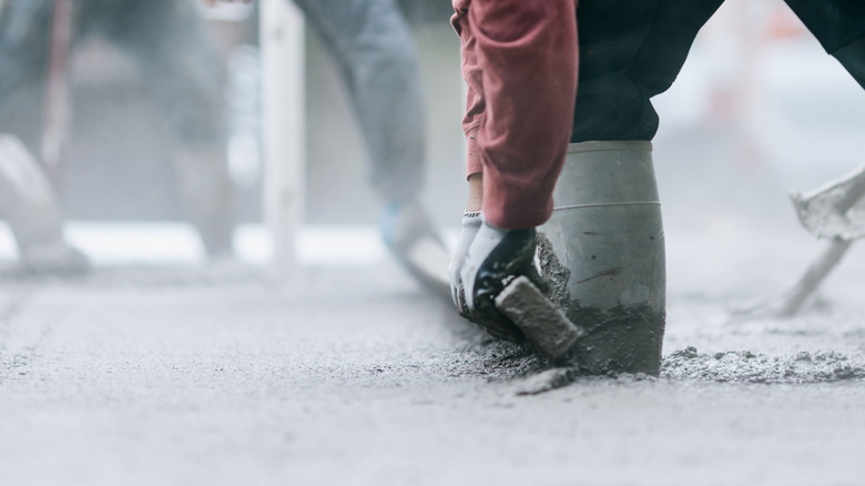 Man with gloves and boots on pouring concrete onto ground and levelling