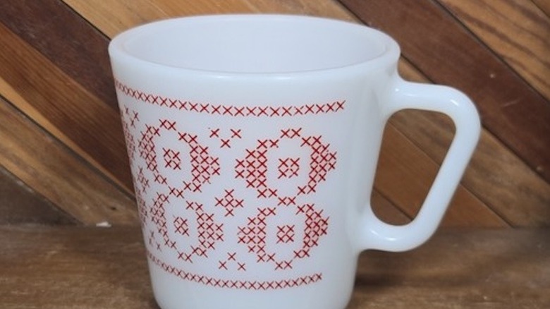 Close-up of a cross-stitch Pyrex mug with a wood background.