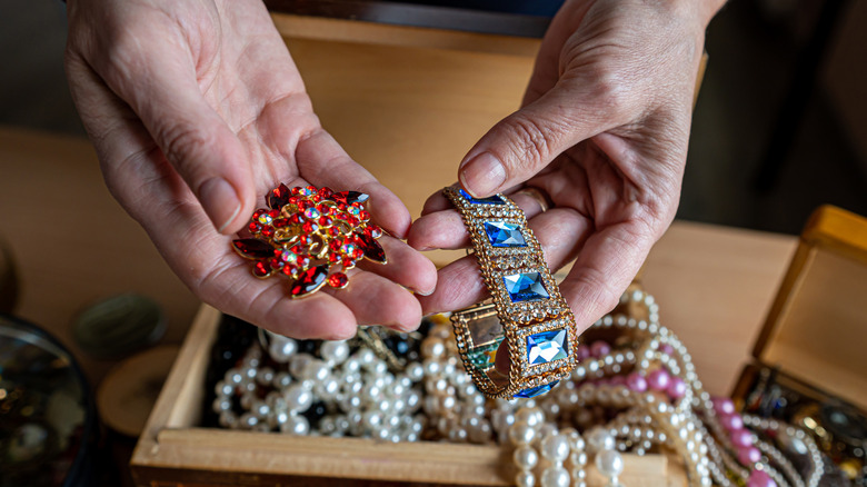 A person holds vintage costume jewelry pieces in shades of red and blue.