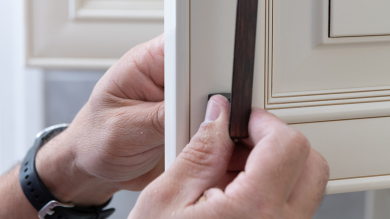 a person fixing the handle on a cabinet.