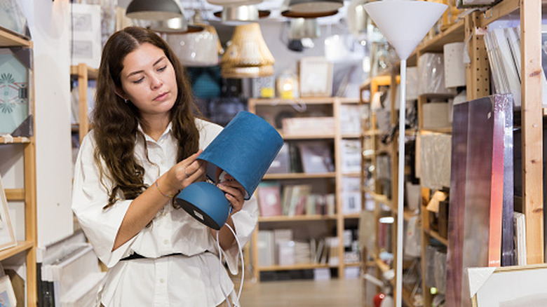 Young woman examining blue contemporary lamp at store with many lamps and lampshades