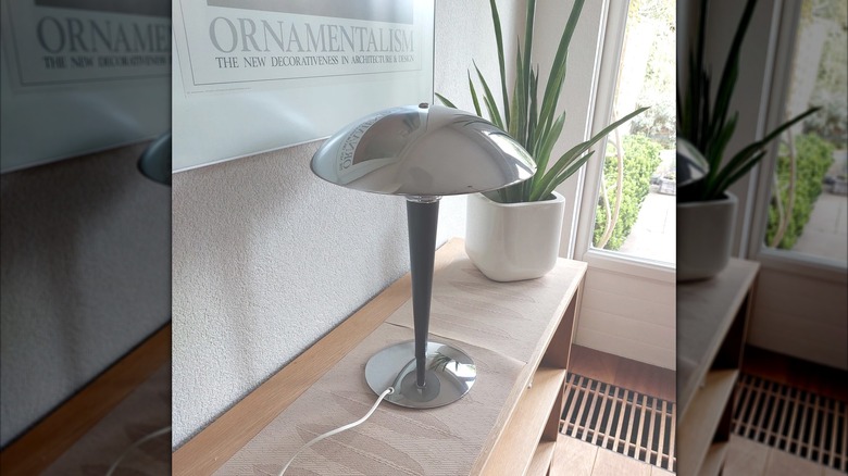 Vintage art deco chrome-plated mushroom lamp plugged in on low wooden shelf beside modern plant and decor
