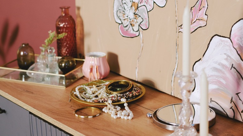 jewelry on a dresser with floral wallpaper behind