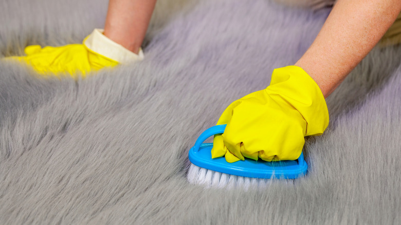 woman brushing faux fur with a scrub brush and yellow gloves