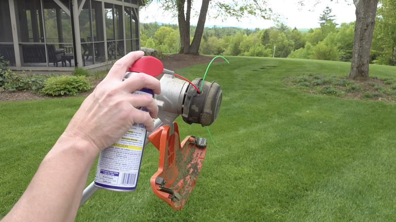 Hand spraying WD-40 in weed whacker in backyard setting.