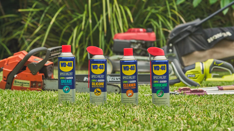Four cans of WD-40 lined on a lawn in front of gardening tools