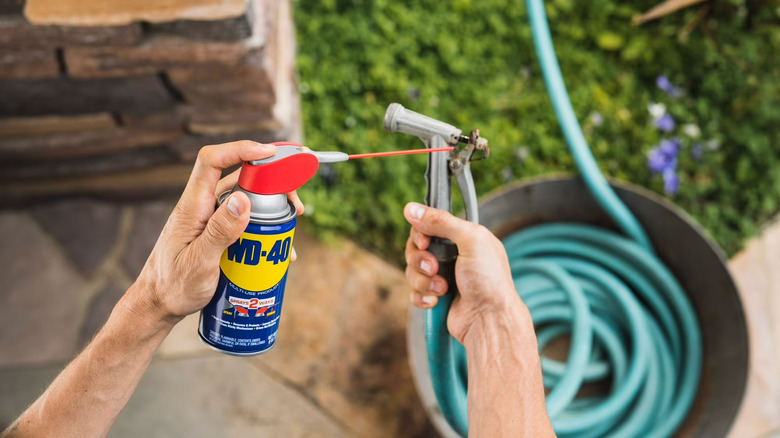 A man's hands spraying WD-40 on the end of a garden hose nozzle