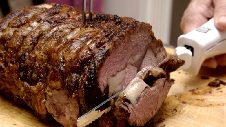 Person carving a roast with an electric knife on a cutting board