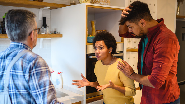 A couple looks frustrated with a repairman in their kitchen