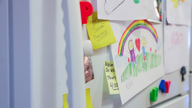 kids artwork, alphabet magnets, and sticky note reminders cluttering a white fridge