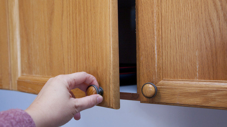 Hand opening a honey oak kitchen cabinet