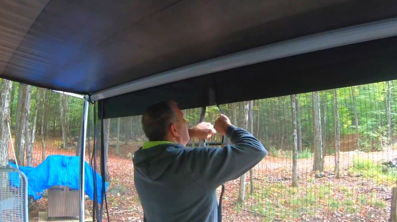 Man installing magnetic screen doors as affordable patio screen with wooded backyard.