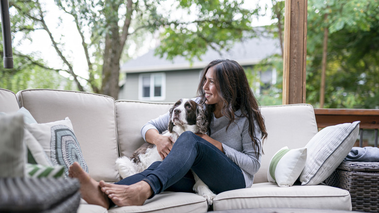 Woman smiling and sitting with dog on outdoor patio with no screen.