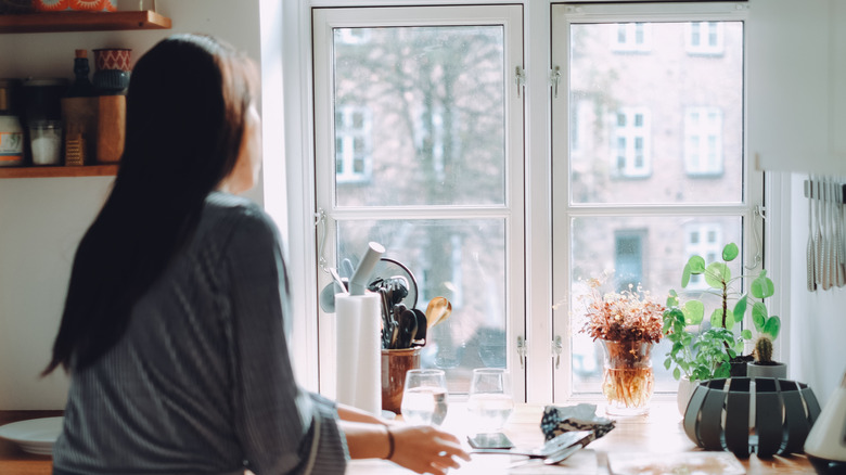 Woman looking out bright clear window while doing chores inside of her private home