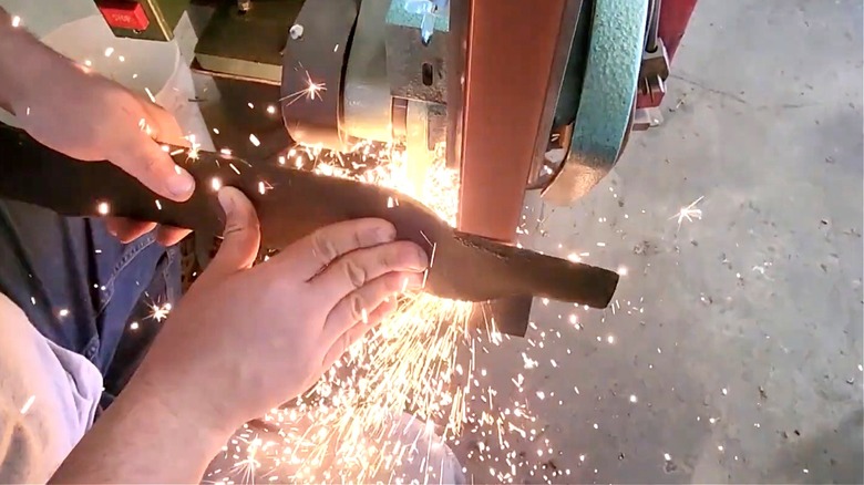 A man sharpening a lawn mower blade using stationary belt sander.