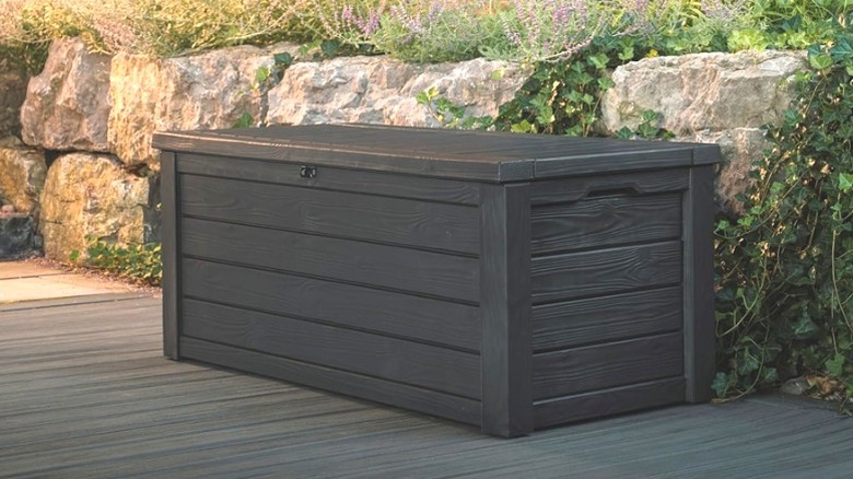 Keter Westwood Deck Box on concrete patio in front of short stone wall
