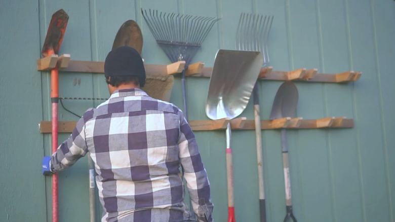 Man putting long-handled garden tools on a DIY wall-mounted outdoor rack