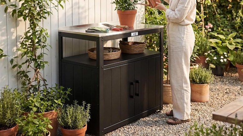 Woman watering plant on top of Feasto Metal Outdoor Potting Bench in garden