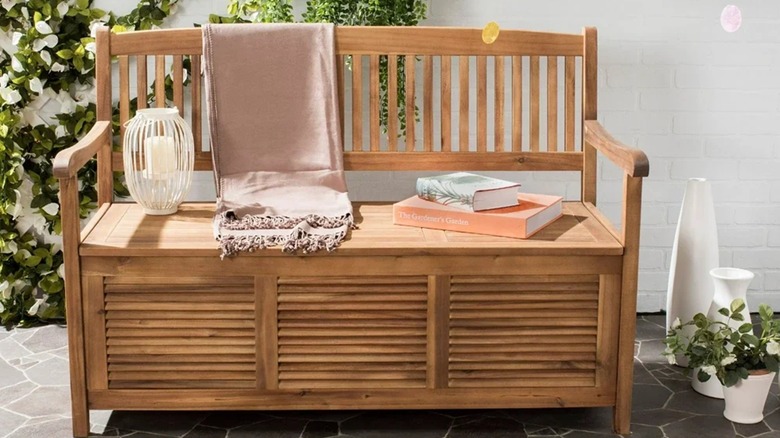 One Allium Way Acacia Outdoor Bench on sunny patio with white wall background