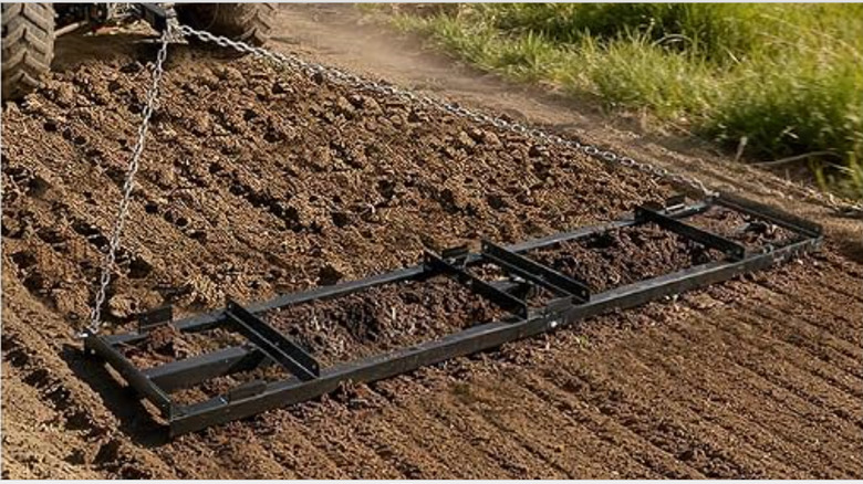 A tractor pulling a drag harrow to smooth a gravel surface.