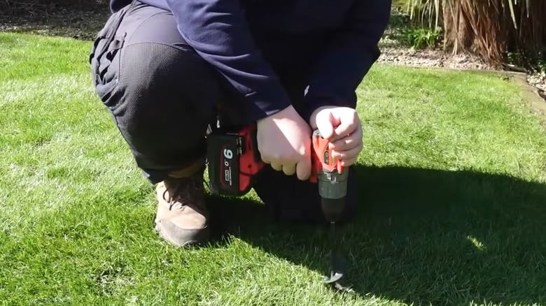 Man drilling into lawn with long bulb-planting drill bit to aerate it