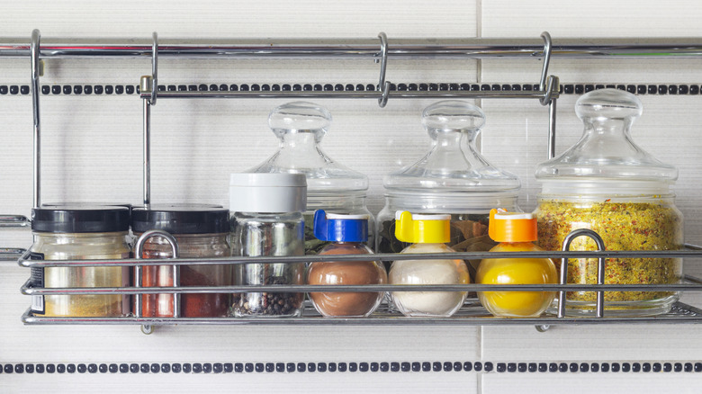 A wired spice rack with jars of spices on a white kitchen wall