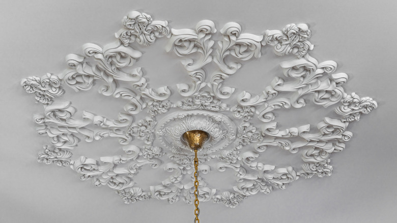 Gold light fixture hanging from ornate plaster ceiling medallion.